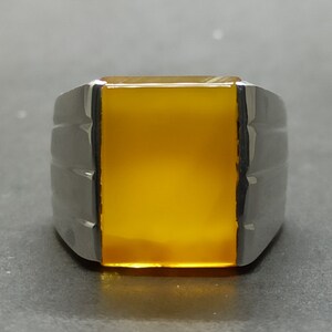 May include: A silver ring with a yellow gemstone. The ring has a rectangular shape and a smooth, polished finish.