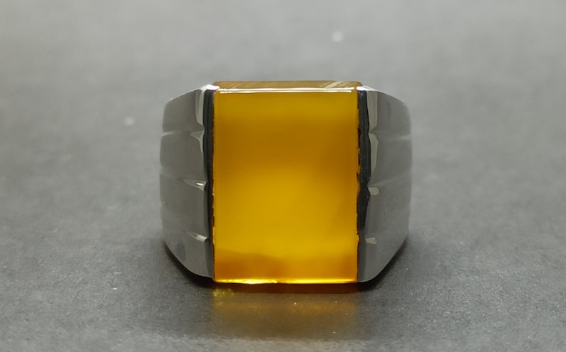 May include: A silver ring with a yellow gemstone. The ring has a rectangular shape and a smooth, polished finish.
