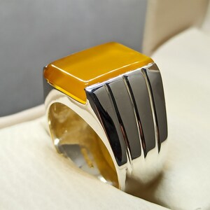 May include: A silver ring with a yellow gemstone. The ring has a wide band with three grooves.