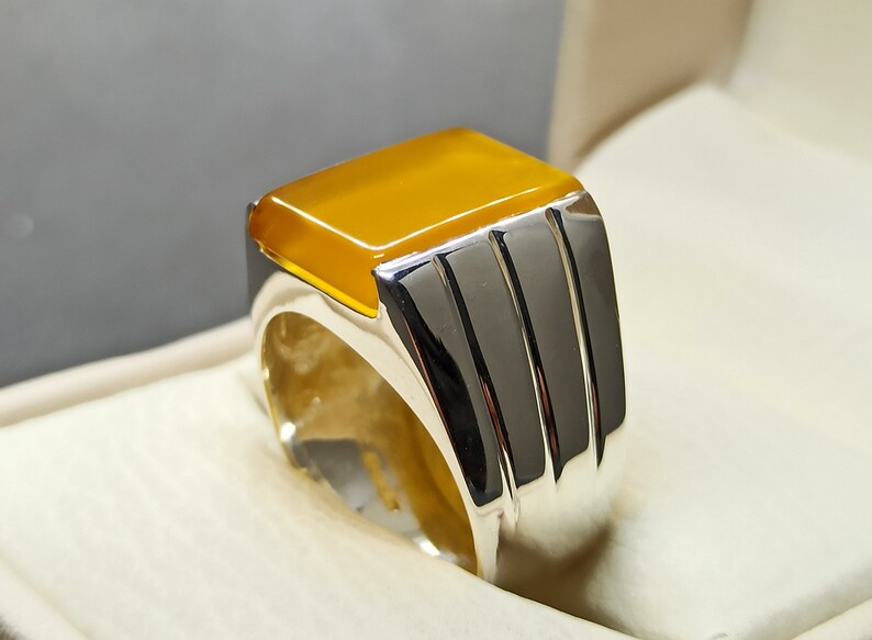 May include: A silver ring with a yellow gemstone. The ring has a wide band with three grooves.