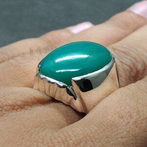 May include: A silver ring featuring a large, oval-shaped green gemstone.