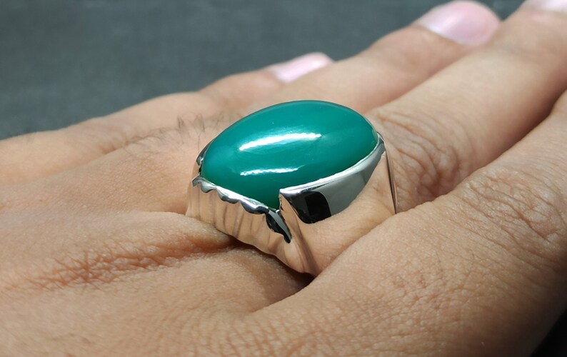 May include: A silver ring featuring a large, oval-shaped green gemstone.