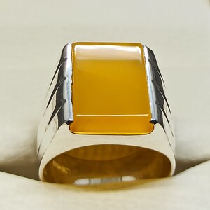 May include: A silver ring with a yellow gemstone. The ring has a square-shaped setting and a textured band.