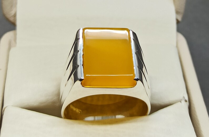 May include: A silver ring with a yellow gemstone. The ring has a square-shaped setting and a textured band.