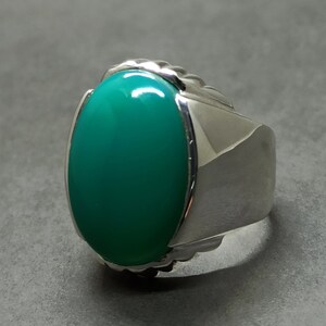 May include: A silver ring featuring a large, oval green gemstone set in a textured band.