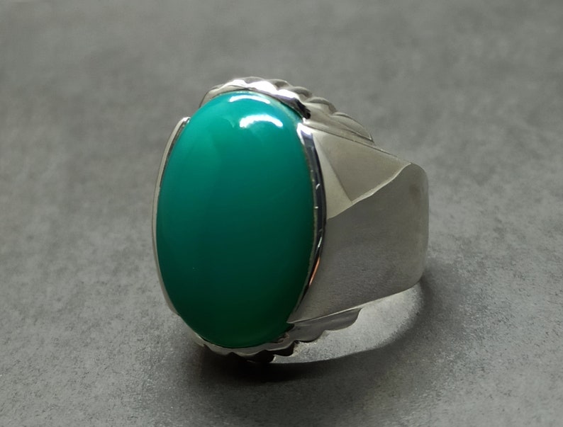 May include: A silver ring featuring a large, oval green gemstone set in a textured band.