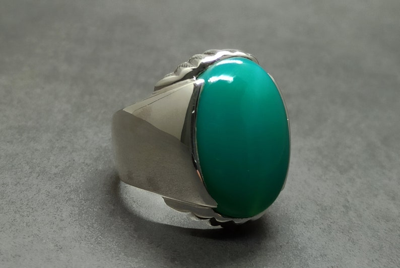 May include: A silver ring with a large oval green gemstone set in a textured silver band.