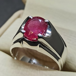 May include: A silver ring with a large, oval-shaped ruby gemstone. The ruby is a deep red color and has a smooth, polished finish.