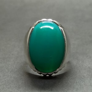 May include: A silver ring featuring a large, oval-shaped green gemstone.