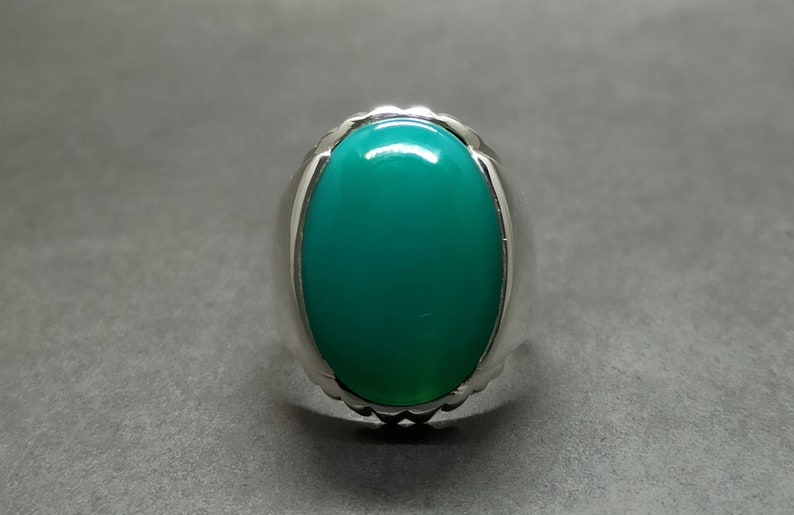 May include: A silver ring featuring a large, oval-shaped green gemstone.