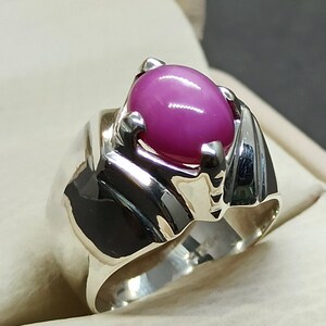 May include: A silver ring with a pink oval gemstone set in a claw setting. The ring has a wide band with a textured design.