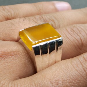 May include: A silver ring with a yellow gemstone. The ring has a rectangular setting with a smooth, polished finish.