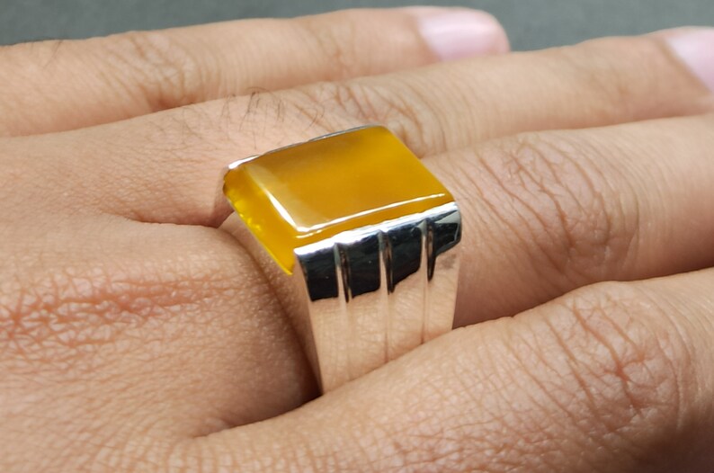 May include: A silver ring with a yellow gemstone. The ring has a rectangular setting with a smooth, polished finish.
