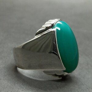 May include: A silver ring with a large oval green gemstone. The ring has a textured band.