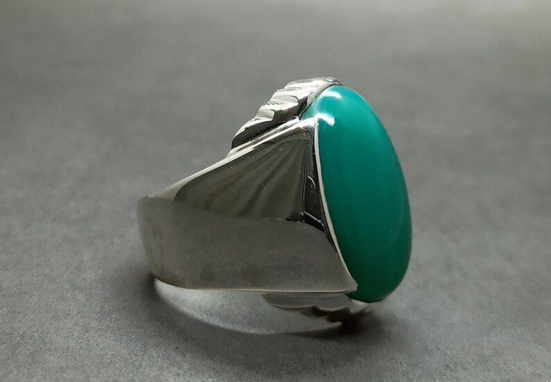 May include: A silver ring with a large oval green gemstone. The ring has a textured band.
