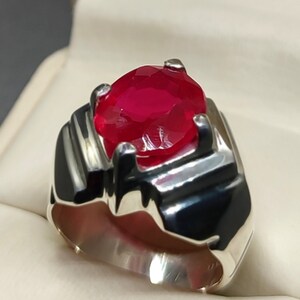 May include: A silver ring with a large, oval-shaped, red gemstone.