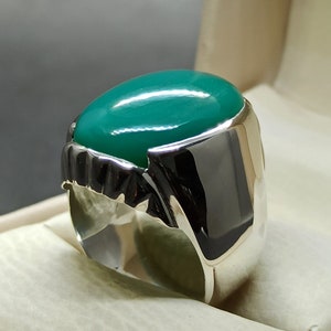 May include: A silver ring featuring a large, oval-shaped green gemstone. The ring has an intricate design around the stone.