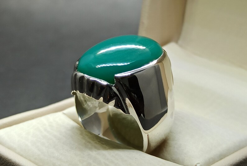 May include: A silver ring featuring a large, oval-shaped green gemstone. The ring has an intricate design around the stone.
