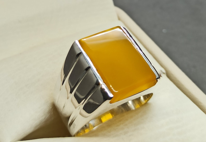 May include: A silver ring with a yellow gemstone. The ring has a textured band.