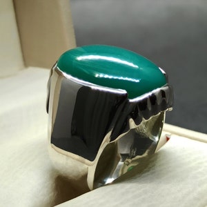 May include: A silver ring featuring a large, oval-shaped green gemstone. The ring has a detailed, textured band.