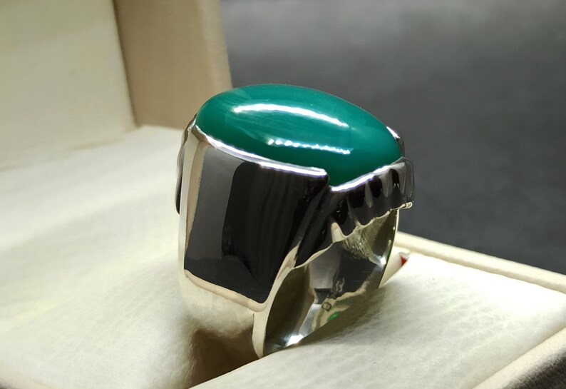 May include: A silver ring featuring a large, oval-shaped green gemstone. The ring has a detailed, textured band.