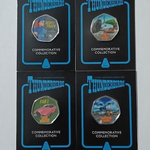May include: Four commemorative Thunderbirds coin cards. Each card features a coin with a different image and the words "Thunderbirds" and "Commemorative Collection". The coins depict Scott Tracy, a scene with a vehicle, FAB 1, and a scene with a helicopter.