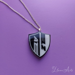 May include: A silver chain necklace with a black and white shield pendant featuring the text "AEZ".