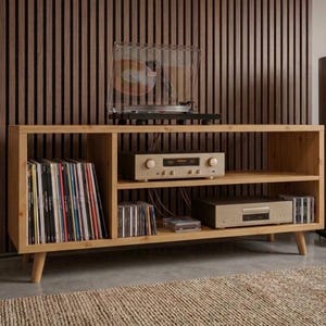 May include: A light-toned wooden media console with tapered legs, featuring open shelving filled with vinyl records and compact discs. A turntable sits on the top surface, while an amplifier and a CD player are placed on the interior shelves.