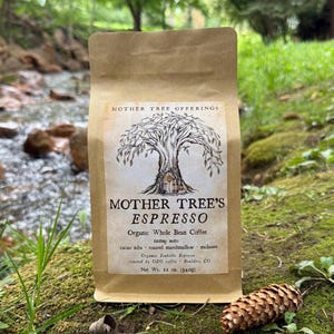 Peut inclure: Un sachet de café en papier beige étiqueté Mother Tree Offerings Mother Tree's Espresso Organic Whole Bean Coffee avec des notes de dégustation de grué de cacao, guimauve grillée et mélasse. L'étiquette inclut une illustration d'arbre et 340g.