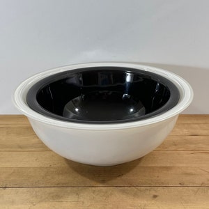 May include: A round mixing bowl featuring a smooth white exterior and a contrasting glossy black interior. The bowl has a wide, slightly flared rim and a deep, curved basin, presenting a clean, two-tone design suitable for kitchen use.