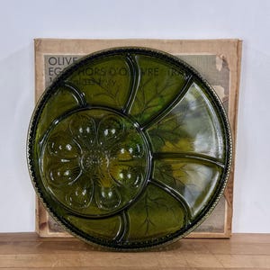 May include: A round, dark green glass serving tray featuring a central circular section with eight egg-shaped indentations surrounded by a larger outer ring divided into four curved compartments, each embossed with a delicate leaf vein pattern.