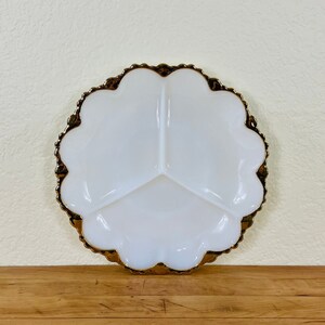May include: A round white milk glass divided serving dish with three distinct sections. The plate features a scalloped edge finished with a metallic gold trim that follows the curved perimeter of the dish, creating a decorative border.