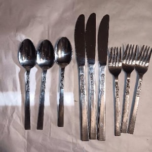 May include: A set of nine stainless steel flatware pieces consisting of three spoons, three knives, and three forks. Each utensil features a polished finish on the head and a textured, decorative pattern on the handle, providing a uniform look.