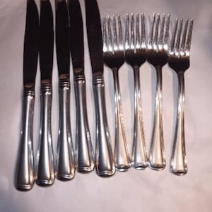 May include: A collection of stainless steel cutlery, comprising six knives and six forks. The knives feature a slender, elongated form with dark blades and silver handles. The forks have a traditional tined design with matching silver handles.