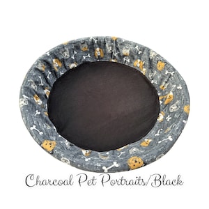 May include: A charcoal gray dog bed with a black, soft, removable liner. The bed is decorated with a pattern of white bones and small, colorful dog portraits.
