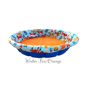 May include: A blue inflatable pool with a soft, orange, and blue fox print lining. The text "Winter Fox/Orange" is printed below the pool.
