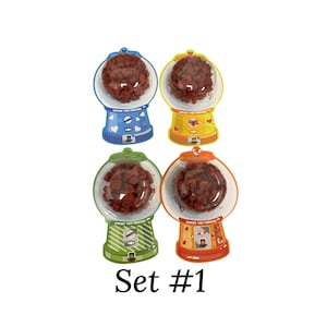 May include: Four colorful gumball machine-shaped containers filled with brown candies. The containers are blue, yellow, green, and orange, each with a unique design. The text "Chew You Forever" is printed on each container. The text "Set #1" is below the containers.