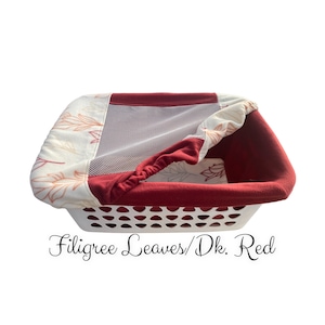 May include: A white laundry basket with a red and white fabric liner. The liner has a mesh top and a pattern of brown leaves. The text "Filigree Leaves/Dk. Red" is printed below the basket.