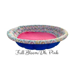 May include: A blue inflatable pool with a pink fabric liner and a white floral print around the top edge. The text "Full Bloom/Dk. Pink" is printed below the pool.