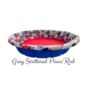 May include: A blue plastic dog bed with a red fleece liner and a gray and red paw print pattern. "Gray Scattered Paws/Red" is written below the bed.