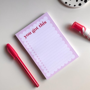 Puede incluir: Un bloc de notas rosa con un borde festoneado y el texto "you got this" en rojo. También hay una pluma roja y un resaltador rosa en la imagen.