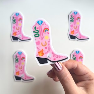 Puede incluir: Cinco pegatinas de botas de vaquero rosas con varios diseños coloridos, incluyendo un arcoíris, una herradura, una serpiente, un corazón, una estrella, un fuego y un dado.