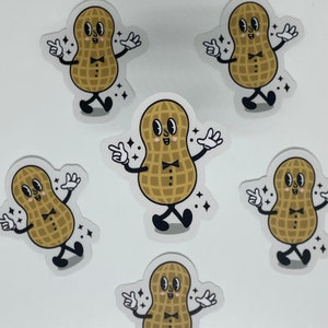 May include: A collection of clear stickers featuring a cartoon peanut character with a bow tie, black shoes, and white gloves. The peanut is light brown with a grid pattern and is surrounded by sparkling star accents.