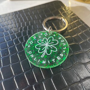 May include: Green glitter keychain with a white four-leaf clover and the text "Unlimited Luck".