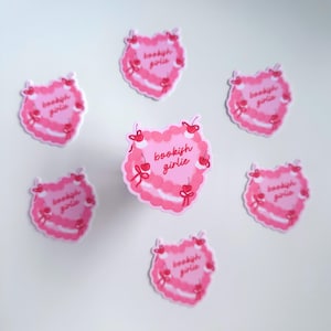 May include: Six pink heart-shaped stickers with the text "bookish girlie" in red cursive lettering. Each sticker features a white lace design and red cherries.