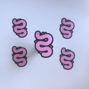 May include: Five pink worm stickers with a black outline and a smiling face. The worms are in a squiggly shape, with a light pink body and a darker pink outline. The stickers are on a white background.