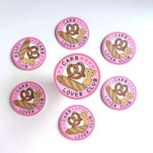 Puede incluir: Seis pegatinas redondas de color rosa y blanco con el texto "Carb Lover Club" y una imagen de dibujos animados de un pretzel, pan y pasta de lazo.