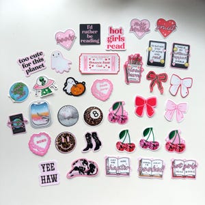 May include: A collection of pink and red stickers with various designs, including hearts, ghosts, books, cherries, bows, and text. The text includes phrases like "too cute for this planet", "hot girls read", "book lover", "just one more chapter", and "sorry fully booked".