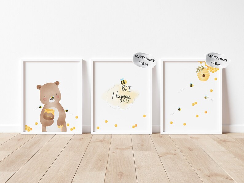 May include: Three white framed prints with a bee theme. The first print features a brown bear holding a jar of honey with bees flying around it. The second print has the text "Bee Happy" with a bee and honeycomb design. The third print has a honeycomb with bees flying around it.