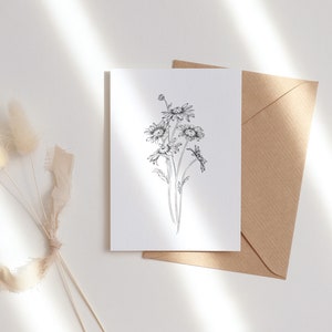 May include: A white card with a black and white line drawing of a bouquet of daisies. The card is sitting on a brown envelope.